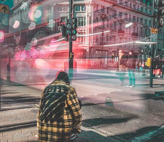 Busy city street with a lone person sitting alone among the movement, lights and chaos.