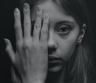 Black and white portrait of a stern-faced girl holding one hand over half of her face.