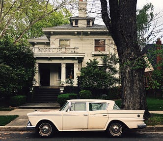 An old-fashioned wooden house with a retro car out front.