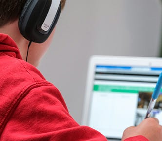 boy wearing headphones taking notes from computer screen