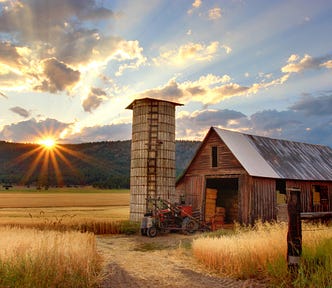 A cozy farm surrounded by fields at sunset