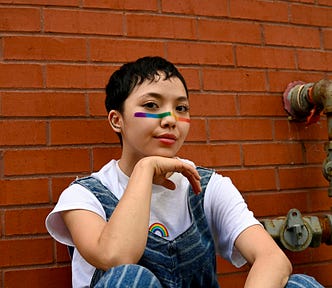 A nonbinary child with very short dark hair and a rainbow on their nose