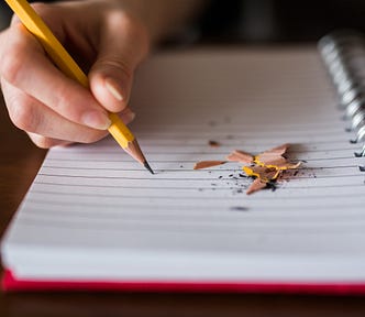 An open notebook someone is writing in and pencil shavings are laying around