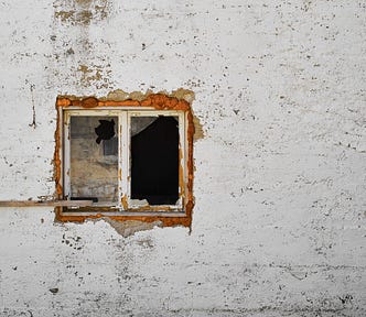 old white concrete wall with paint chipping with a small window slightly off-center