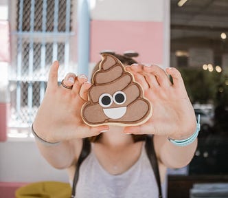 A women holding up a cookie decorated as, and in the shape of, a “poop” emoji