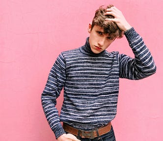 A young boy in a striped shirt scratching his head in confusion.