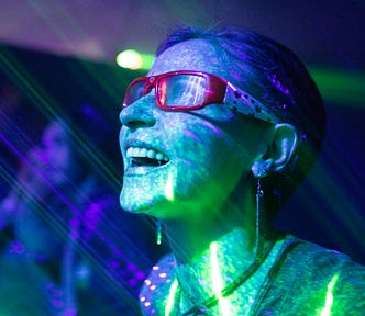 An excited woman stares at a screen, bathed in colorful light