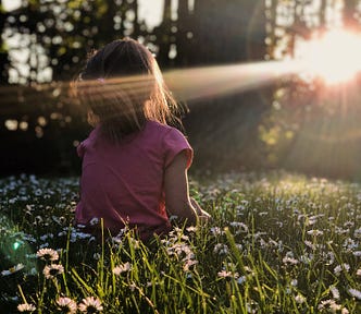 A girl sitting among flowers facing the warm rays of the sun