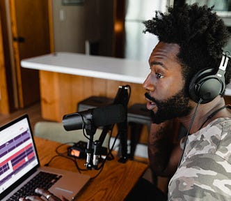 A man sits in front of a laptop, speaking into a microphone.