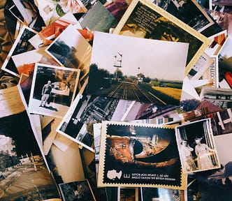 A scattered collection of old photographs and postcards in a mix of color and black-and-white, spread across a surface. The photos include scenes of people, landscapes, railways, and historical artifacts, with one prominent postcard showing the Sutton Hoo helmet from the British Museum. The arrangement evokes a nostalgic and archival feeling, capturing moments from different times and places.