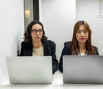 two women on laptops side eyeing each other