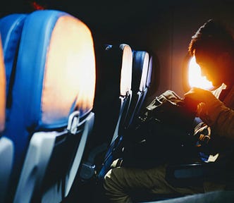 A man searches through his cabin bag on an airplane seat, preparing for takeoff