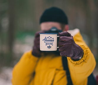 hiker holding a mug with the words “adventure begins”