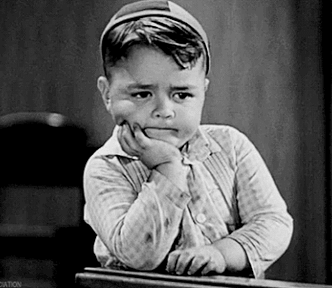 Black and white gif of a young boy with an unhappy expression and fist propping his head up, tapping his fingers against a wooden table.