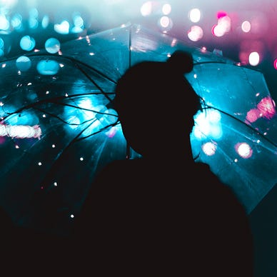 Person silhouetted beneath a clear umbrella. There’s arty purple and blue lighting in the background.