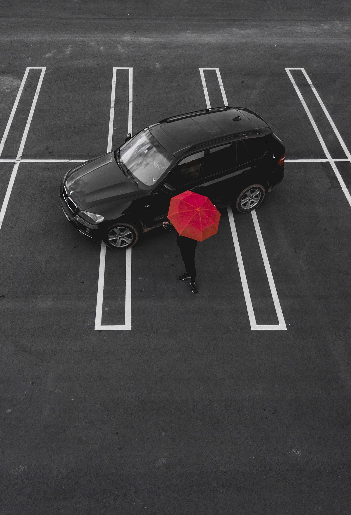 A black SUV in an empty parking lot with a person holding a red umbrella next to it.