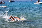 Two swimmers in the ocean racing shoulder to shoulder, with a third swimmer behind.