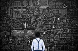 A man standing in front an oversized blackboard with a chaotic overload of information drawn representing a data chaos.