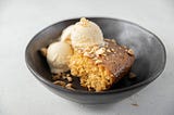 Image shows a piece of cake in a bowl with two scoops of ice cream next to it.