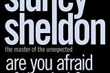 Image of book cover of Sidney Sheldon’s ‘Are you afraid of the dark?’. The image shows a silhouette of a woman staring outside a window.