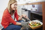 Woman putting tray of roast vegetables in oven