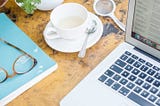 A laptop with tea and a notebook and glasses