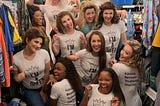 A group of young girls, wearing shirts saying “I’m a Queen” pose, smile, and laugh.