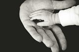 A child’s small hand rests in an adult’s larger hand.
