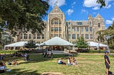 College campus with students on a grass lawn in front of a majestic stone building