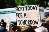 a cardboard protest sign in a crowd that says “Fight today for a better tomorrow”