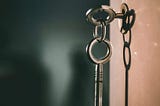 Two brushed silver skeleton keys; one inserted into the keyhole, the other hangs from the shared keyring.