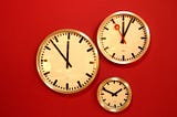 Three analog clocks of various sizes positioned against a red background.