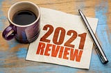 review of 2021 written on a napkin, alongside a cup of black coffee and a pen