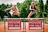 Two women jumping over a hurdle with “House For Sale” sign attached