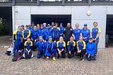 A group of people in blue and yellow sportswear are posing for a photo outside a building with a large shutter door.