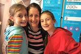 Steph, dark haired mum, with an arm round each of her girls, aged 9 and 11. All are smiling at the camera