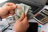 Businessman counting hundreds of dollars at his table.