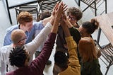 Image shows a diverse group of people in business attire doing a group high-five. Using Personality Profiles to Boost Growth.