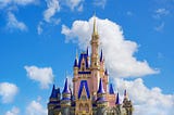 View of Cinderella’s Castle at Magic Kingdom in Orlando, Florida, with its iconic spires and turrets bathed in vibrant colors under a clear blue sky