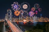 Ten fireworks exploding above a city skyline at night, with a bridge in the foreground
