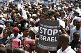 Photo of a protest with a large black and white sign that reads “Stop Israel: Stop Israeli Terror.”