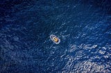 Featured image: An aerial photograph of a rubber dinghy alone on the deep blue open ocean.