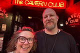 Me standing outside the legendary Cavern Club in Liverpool, smiling under the glow of the red neon sign. Next to me is a serious-faced bouncer in black, guarding the entrance to one of the most iconic music venues in the world. Beatles energy in the bricks.
