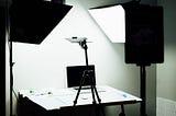 Laptop on a table surrounded by two studio lights. There is a white backdrop behind the table.