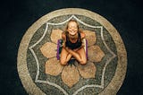 Yoga & Eastern Influence on Holistic Healthcare, photo of a young women, very flexible, sitting in a lotus position, on a lotus mandala designed on a floor.