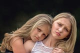 A girl embraces her frowning sister