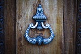 A closed wooden door with a brass knocker, representing institutional access and support that exist but not necessarily available