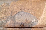 A desert landscape with sandstone arch is seen overlaid on the salt-crusted rear window of a hatchback automobile.