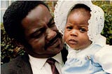 Black man holding Black baby who is looking at the camera