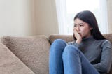 Close up face of unhappy asian pretty young woman sitting alone on couch